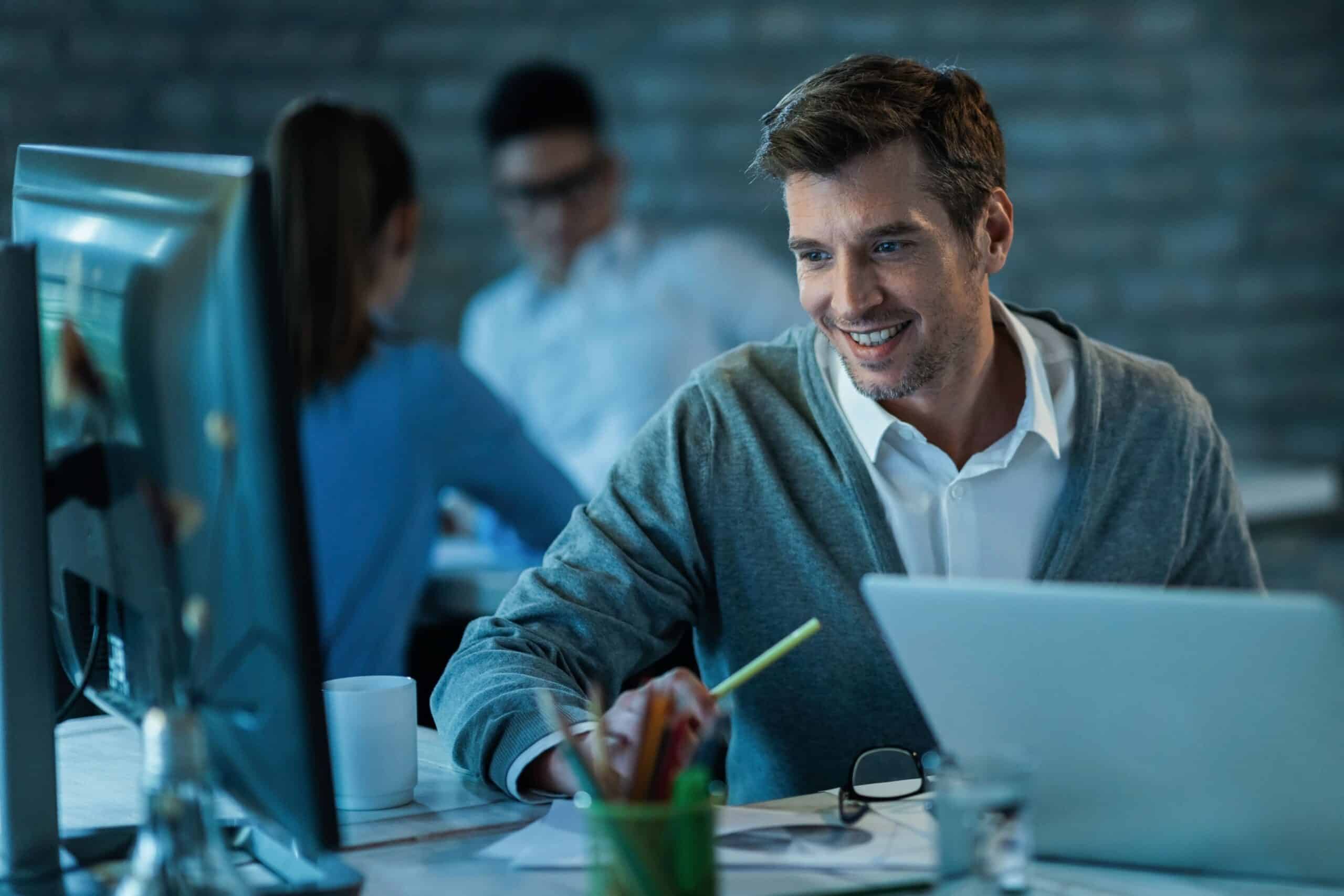 Homem sorrindo trabalhando no computador enquanto faz uma videochamada.