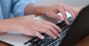 mão feminina mexendo em um computador em cima da mesa, ângulo lateral.