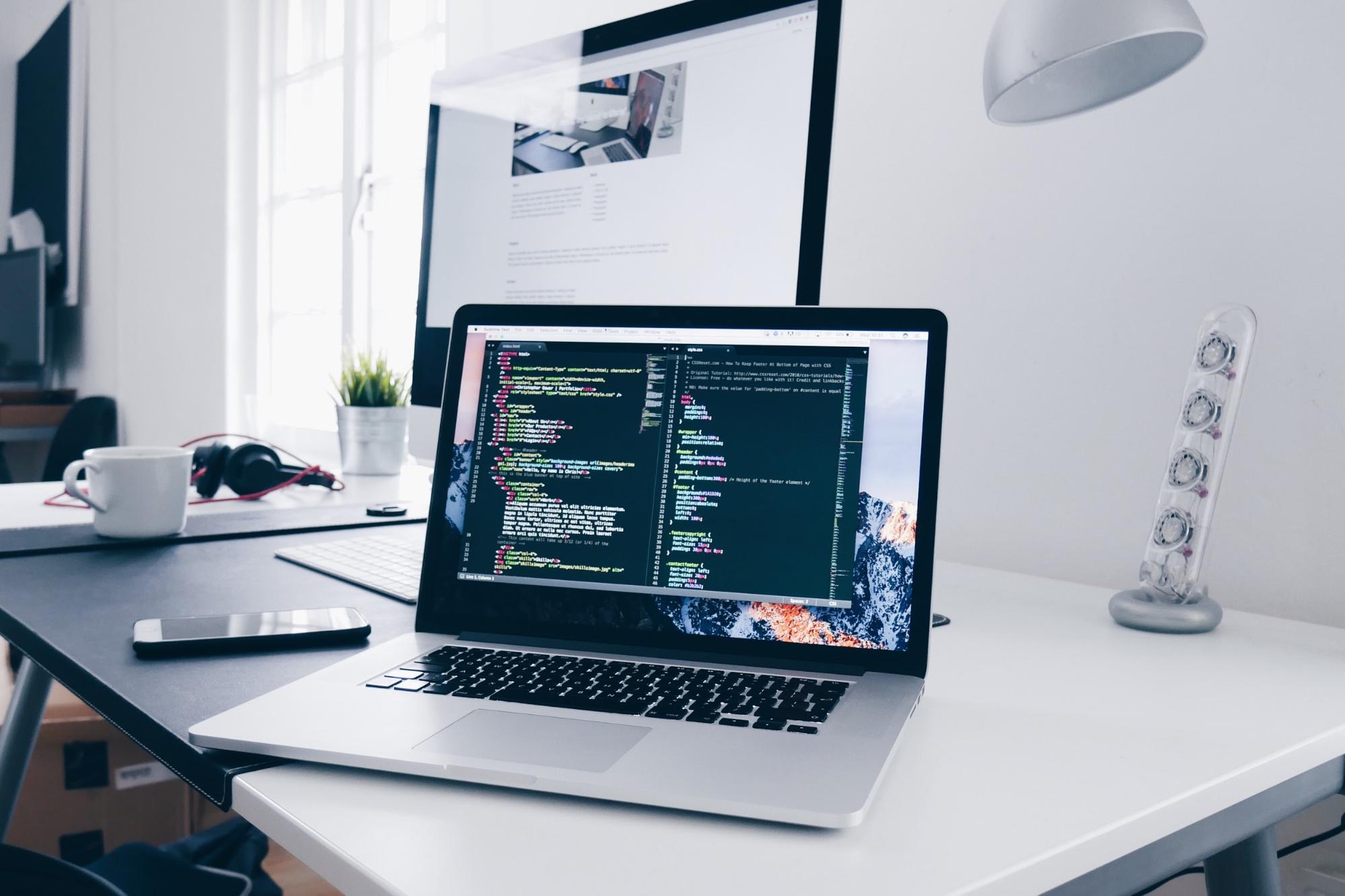 Computador com código de programação em cima de uma mesa.