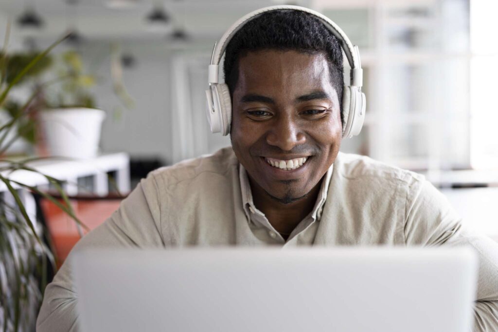 Um homem usando fones de ouvido sorri enquanto olha para a tela de um laptop, sentado em um espaço moderno e iluminado, com plantas ao fundo, enquanto se prepara para comprar um certificado digital on-line.
