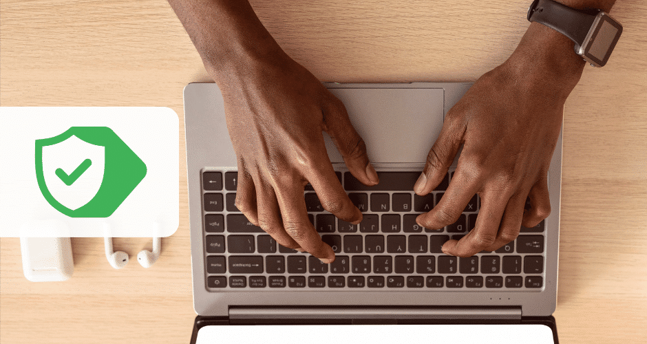 na imagem, duas mãos de um empresário, pele negra, digitando em um computador, ao lado um fone de ouvido bluetooth.