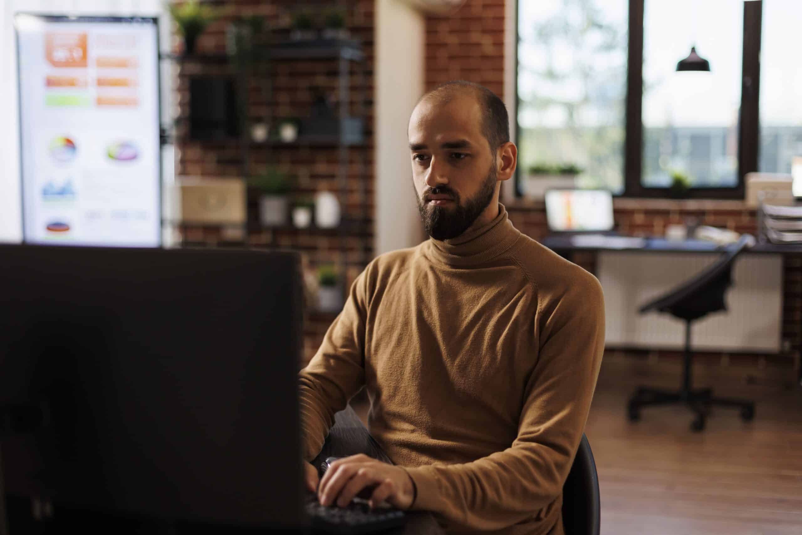 Homem vestido casualmente trabalhando no computador no seu ambiente home office.
