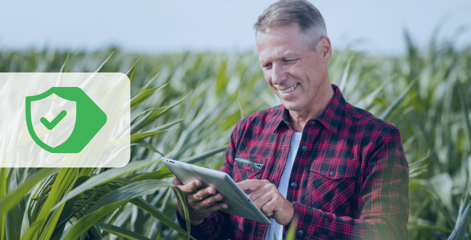 Um homem de camisa xadrez está em um campo de plantações altas, sorrindo e usando um tablet. Isso representa como a certificação digital aumenta a segurança nas operações de agronegócio.