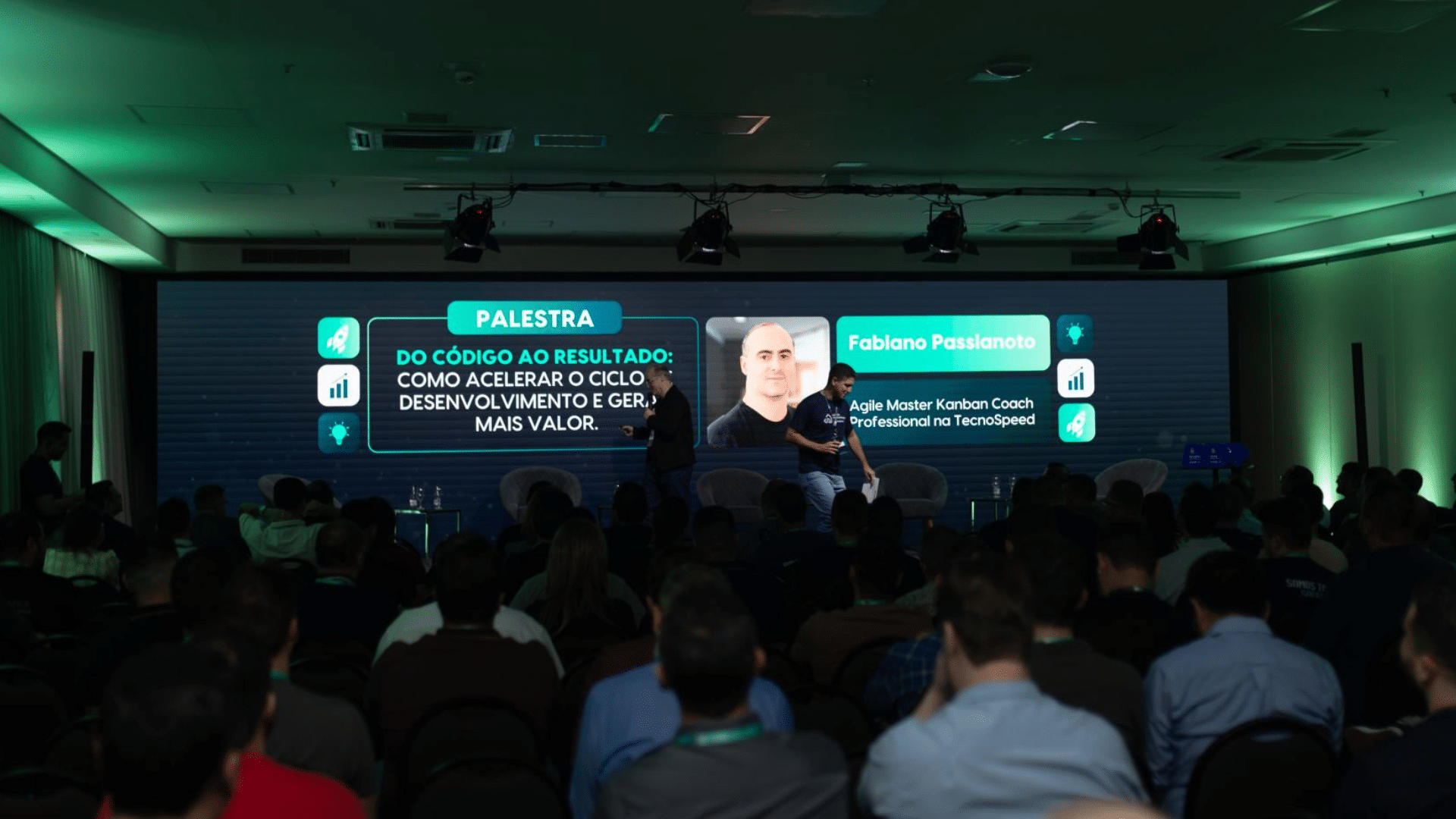 Uma conferência se desenrola com público fixado em um palco onde o palestrante, Fabiano Passalacqua, aprofunda a "Palestra: Do Código ao Resultado - Como Acelerar o Ciclo, Desenvolvimento e Gerar Mais Valor" utilizando metodologia ágil e técnicas como Kanban para aumentar a eficiência e entregar maior valor.