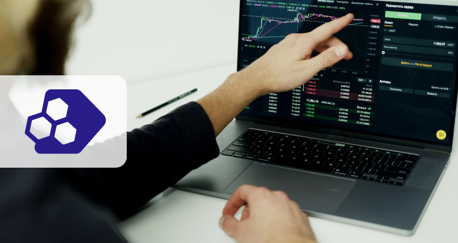 Uma pessoa aponta para gráficos e dados financeiros em uma tela de laptop, analisando tendências do mercado de ações ou criptomoedas ou revisando o perfil do sped fiscal. Um logotipo com três hexágonos aparece em primeiro plano no lado esquerdo da imagem.