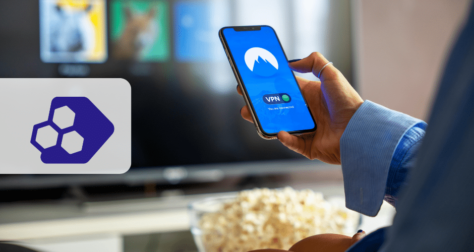 Uma pessoa segurando um smartphone com um aplicativo VPN API NFCom aberto em frente a uma tela de TV; uma tigela de pipoca está próxima. À esquerda, há um logotipo de tecnologia hexagonal roxo em um fundo cinza.