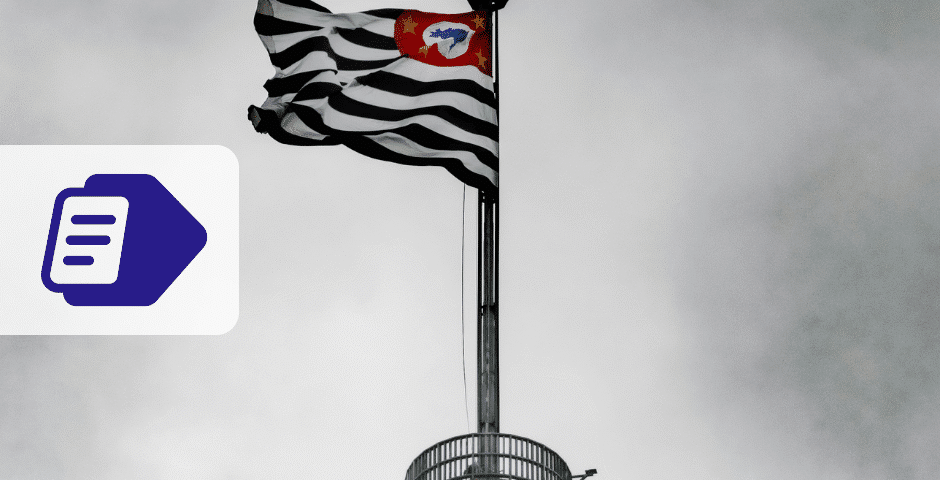Uma bandeira listrada em preto e branco com um emblema vermelho tremula no topo de um mastro contra um céu nublado, fazendo referência a São Paulo. À esquerda, um ícone de documento roxo e branco da NFS-e de São Paulo se destaca na imagem.