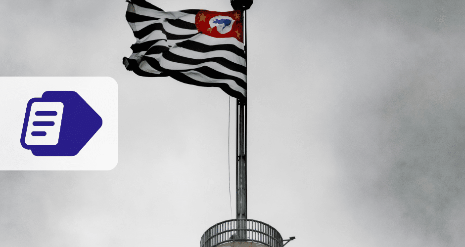 Uma bandeira listrada em preto e branco com um emblema vermelho tremula no topo de um mastro contra um céu nublado, fazendo referência a São Paulo. À esquerda, um ícone de documento roxo e branco da NFS-e de São Paulo se destaca na imagem.