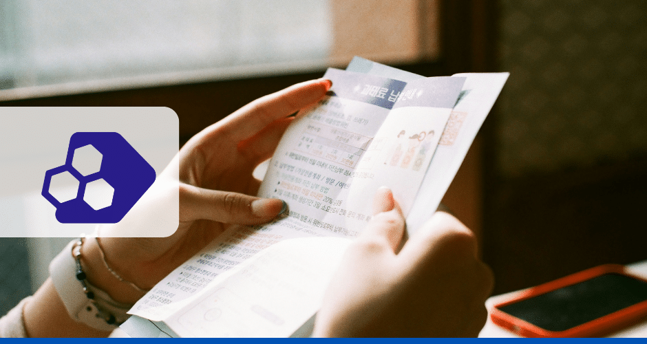 Uma pessoa segura e lê um folheto com texto em coreano perto de uma janela. Um logotipo hexagonal azul abstrato está à esquerda, e um smartphone vermelho está sobre a mesa ao fundo, apresentando informações sobre Notas Fiscais de Débito e Crédito.