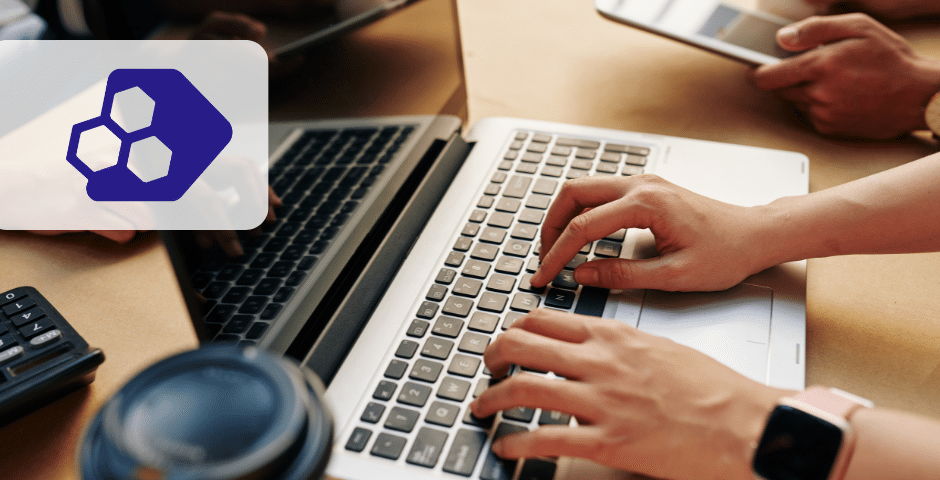 Uma pessoa digita em um teclado de laptop em uma mesa com uma bebida e uma calculadora por perto, possivelmente trabalhando na EFD-Reinf RRA e deduções, enquanto outra usa um tablet. Um logotipo hexagonal azul e branco é sobreposto no lado esquerdo da imagem.