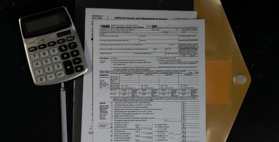 Uma calculadora, formulários de impostos e uma pasta preta com um envelope de arquivo amarelo são colocados em uma superfície escura, sugerindo cálculo de impostos ou trabalho financeiro.