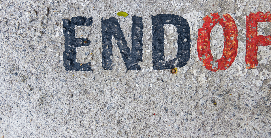 Close-up de um texto pintado sobre concreto bruto, mostrando a palavra “END” em preto e parte de outra palavra que começa com “OF” em vermelho — possivelmente fazendo referência a frases como “Fim do ICMS” —, com o restante da mensagem cortado.