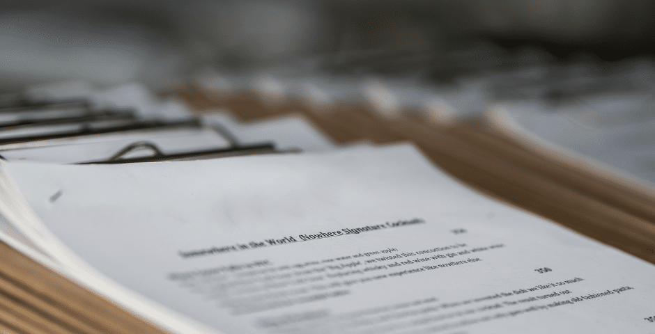 Uma pilha de papéis presos em pranchetas, com o texto visível, mas fora de foco, sugerindo que se trata de documentos relacionados ao Ajuste SINIEF 49/2025, prontos para revisão ou distribuição.